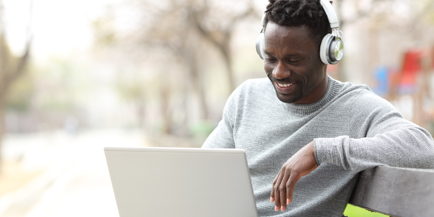 Black Man Outside On Bench Connecting On Laptop