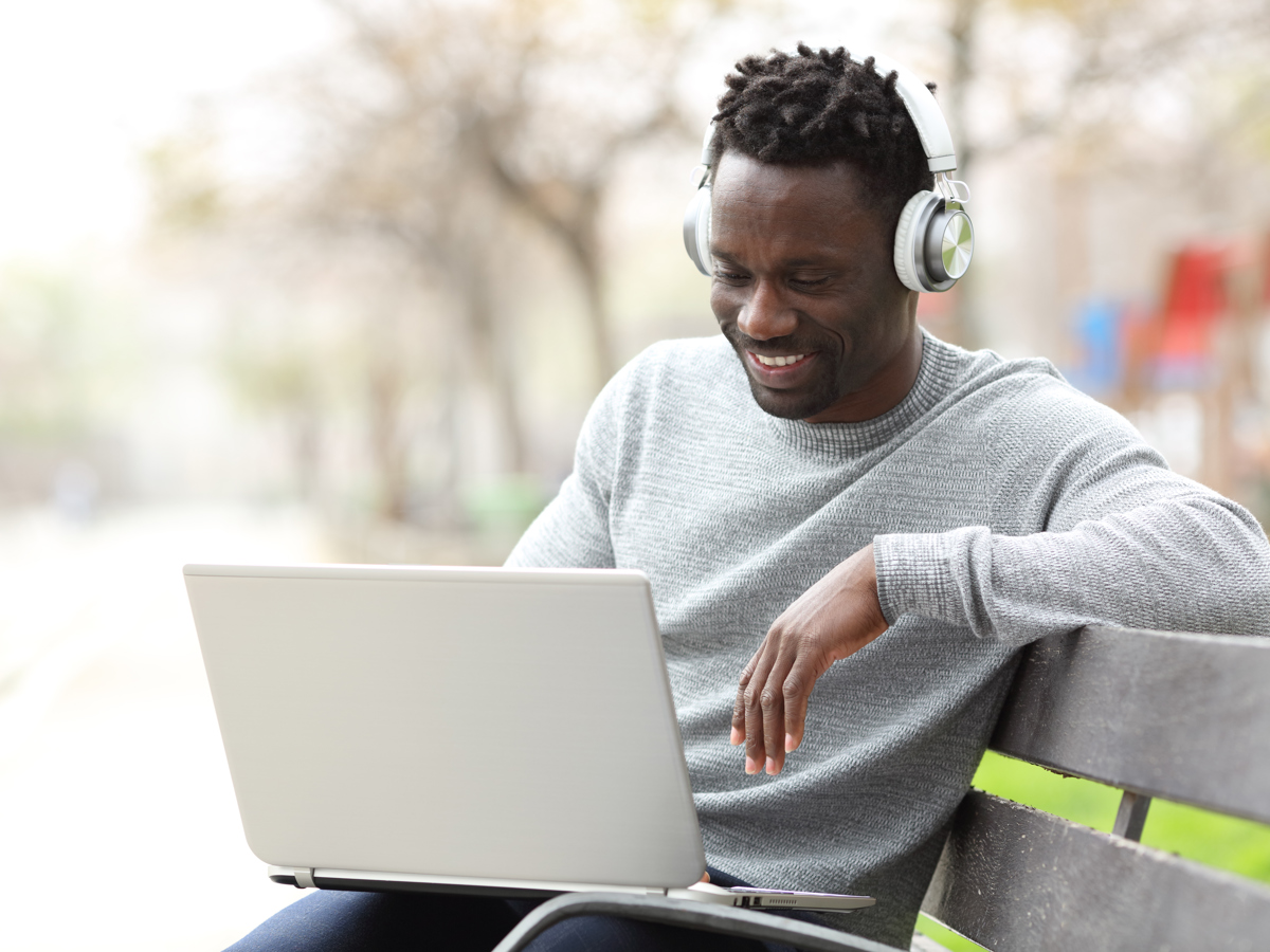 Black Man Outside On Bench Connecting On Laptop